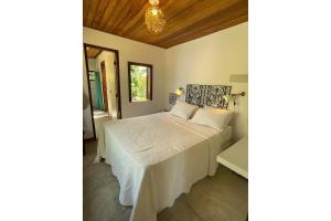 a bedroom with a bed with white sheets and a chandelier at Casa do Mangue-Paraíso na beira do rio Wi-Fi 300 M in Jaguaripe