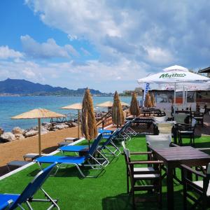 un gruppo di sedie, tavoli e ombrelloni su una spiaggia di Point Ephemere Beachfront Apartments a Città di Zante