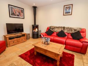 a living room with a red couch and a coffee table at Cow Byre in Little Tew
