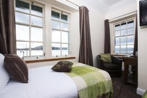 a bedroom with a bed and a chair and windows at North Kessock Hotel in Inverness