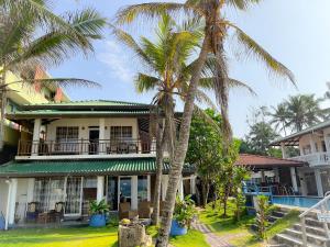 una casa con palmeras delante en Pearl Island Beach Hotel, en Hikkaduwa