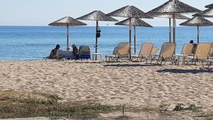 personas sentadas en sillas en la playa bajo sombrillas en ammos seafront family apartments, en Nea Plagia