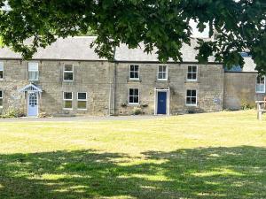 a large stone building with a blue door and a grass field at Blue House Cottage in Elsdon