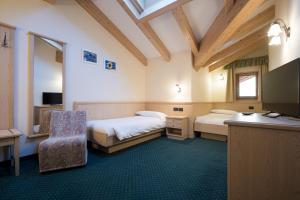 a room with two beds and a desk and a television at Hotel Crepei in Pozza di Fassa