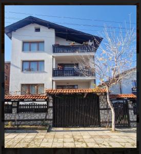 a white building with a black fence and a tree at Къща за гости Карасански in Bansko