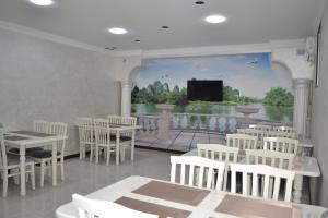 a dining room with white tables and chairs and a mural at Art Angren Hotel in (( Sotsgorod ))