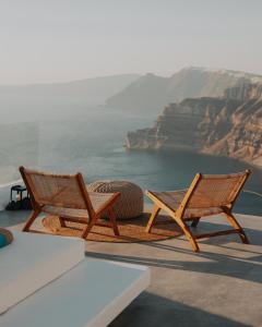 Dos sillas de mimbre sentadas en una cornisa con vistas al océano en Nelya Suites, en Megalokori