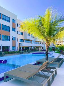 a palm tree and lounge chairs in a swimming pool at Guarajuba Paraíso dos Coqueiros in Guarajuba