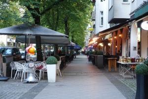 un trottoir avec des tables, des chaises et un parasol dans l'établissement Ferienunterkunft im Tegelhaus, à Berlin