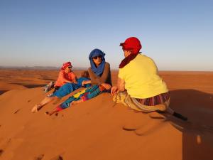 tres personas sentadas en una duna de arena en el desierto en Sahara Peace camp en Zagora