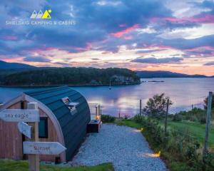 a small building sitting on the side of a body of water at Sunset Cabin- glass frontage luxury couples cabin. in Shieldaig
