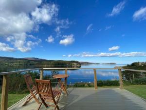 balcón con 2 sillas, mesa y vistas al lago en Sunset Cabin- glass frontage luxury couples cabin., en Shieldaig