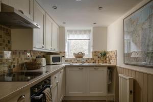 a kitchen with white cabinets and a sink and a window at Swan Cottage in Llangelynin