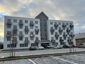 un grand bâtiment blanc avec des voitures garées dans un parking dans l'établissement Apartman Liptov NP14, à Liptovský Mikuláš