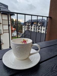 a white cup and saucer on a table with a balcony at Hedonist Zlatibor Mountain Wellness & SPA in Zlatibor