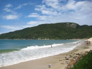 uma praia com pessoas brincando na água e uma montanha em Residence Portal do Santinho em Florianópolis