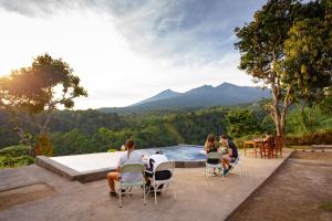 a group of people sitting around a pool with mountains in the background at Pondok Guru Bakti Cottage in Senaru