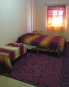 twee bedden in een kamer met een tapijt en een raam bij Habitation Dunes merzouga in Merzouga