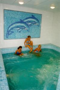 Tres mujeres en una piscina con delfines en la pared en Hárs Thermál Hotel en Gyomaendrőd