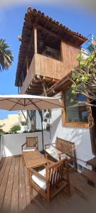 eine Holzterrasse mit 2 Stühlen, einem Tisch und einem Sonnenschirm in der Unterkunft Casa La Aldaba in Los Realejos