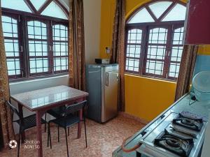 eine Küche mit einem Kühlschrank, einem Tisch und Fenstern in der Unterkunft AlexMarie Holiday Homes Apartments 5 min to Candolim Beach in Candolim