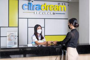 una mujer con una máscara facial le da la mano a un cliente en un mostrador de atención al cliente en Hotel Citradream Semarang, en Semarang
