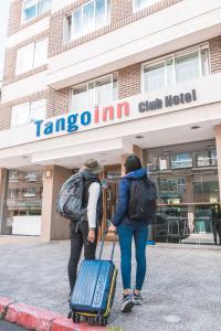2 persone con bagaglio che cammina davanti a un edificio di Tangoinn Club Hotel a San Carlos de Bariloche