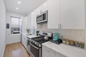 La cuisine est équipée de placards blancs et d'un four avec plaques de cuisson. dans l'établissement Chic Industrial Home In City Center, à Hoboken