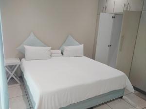 um quarto com uma cama branca com lençóis e almofadas brancos em Posh 2 em Durban