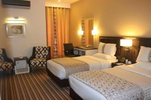 a hotel room with two beds and a chair at West Inn Hotel Faisalabad in Faisalabad