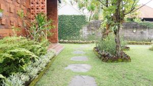 un jardín con una pasarela de piedra y un árbol en Louto Dmell Guesthouse, en Sanur