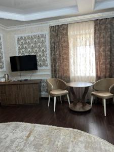 a living room with a tv and a table and chairs at Grand SPA Hotel in Kostanay
