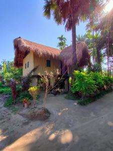 a house with a thatched roof and palm trees at MAHESWAR LAND in Majuli