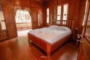 a bedroom with a wooden bed in a room with windows at Joglo Kecombrang Bromo in Ngadisari