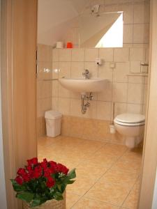 ein Bad mit einem WC, einem Waschbecken und roten Blumen in der Unterkunft Hotel Garni am Schlosspark in Wernigerode