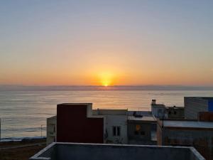 - un coucher de soleil sur l'océan avec un bâtiment dans l'établissement Appartement à louer, à Larache