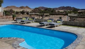 a swimming pool with chairs and a patio with mountains in the background at Elegant Desert Lodge in Sesriem