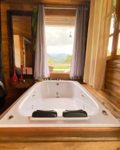 a bath tub in a room with a large window at Pousada Recanto do Lobo Chalés em Urubici in Urubici