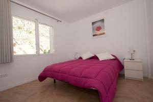 uma grande cama roxa num quarto branco com uma janela em Aparthotel l'Heretat em Cadaqués