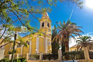 a yellow building with a clock tower and palm trees at Studio apartment in Novalja with sea view, terrace, air conditioning, WiFi 3565-8 in Novalja