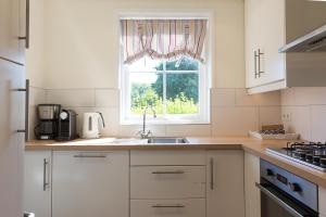 eine weiße Küche mit einem Waschbecken und einem Fenster in der Unterkunft Hello Zeeland - Vakantiehuis Brouwerijweg 43-3 in Domburg