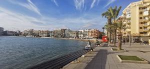 a man sitting on a bench next to the water at Apartament Torrevieja Playa Los Locos in Torrevieja