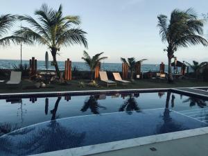 una piscina con palmeras y el océano en Novíssimo Village Beira Mar en Itacimirim