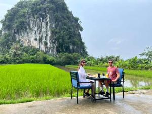 dwoje ludzi siedzących przy stole przed polem ryżowym w obiekcie Tam Coc Horizon Bungalow w mieście Ninh Binh