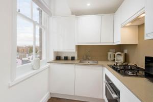 uma cozinha branca com armários brancos e uma janela em Luxury Chelsea Flat em Londres