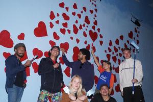 un grupo de personas de pie en frente de una pared con corazones en Lost in San Jose Hostel & Suites, en San José