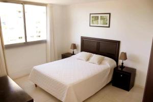 um quarto com uma cama branca e 2 janelas em Blaumer Apartamentos - Edificio Aguila Dorada em Punta del Este