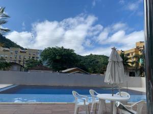 una mesa con sillas y una sombrilla junto a la piscina en Apartamento Guarujá Lazer completo Villa Di Fiori 600mts da praia, en Guarujá