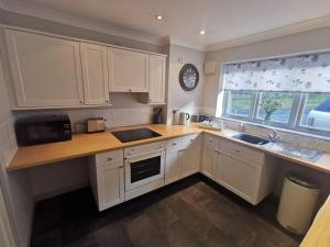 a kitchen with white cabinets and a sink and a window at Twyngaer, a spacious 3 bedroom bungalow sleeps 6 in Knighton