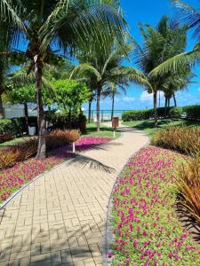 a walkway in a park with pink flowers and palm trees at Apartamento a beira mar com piscina estilo resort in Cabedelo